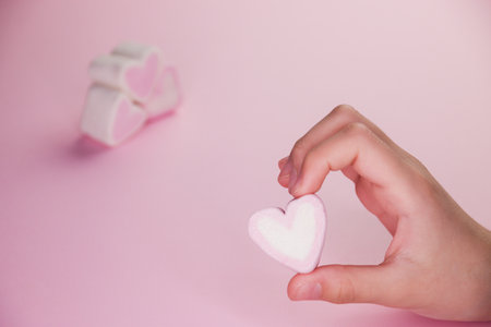 Pastel valentine background made of marshmallows souffle in the form of hearts on a pink background in hands. Valentine's Day concept with copy space.の写真素材