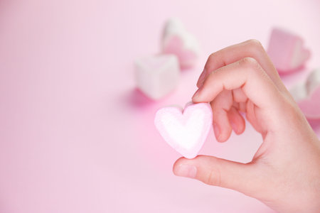 Pastel valentine background made of marshmallows souffle in the form of hearts on a pink background in hands. Valentine's Day concept with copy space.の写真素材