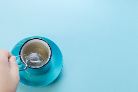 Blue background, strainer and a cup of green tea, a woman's hand makes tea.の写真素材