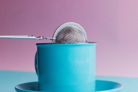 Blue pink background, strainer and a cup of tea.