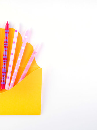 Festive flat lay birthday candles in yellow envelope isolated on white background.