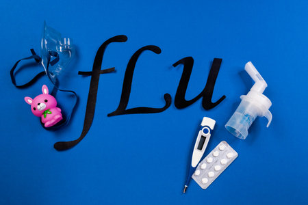 tube mask nebulizer and tubular transparent cable, thermometer, tablets, and the word flu on a blue background, children's colds.の写真素材