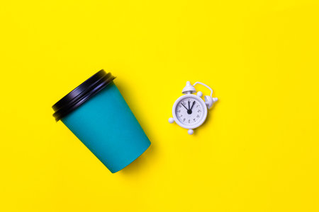 Good morning, Wake up, Wake up concept. Simple flatlay design blue paper coffee Cup and white alarm...
