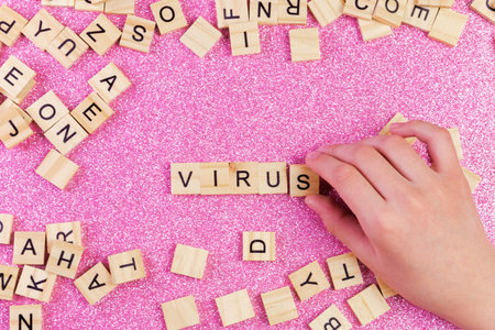 A bunch of wooden letters on the surface of a pink background and a hand made up the word virus, selective focus.の写真素材