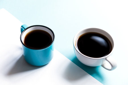Flatlay top view of two coffee cups on white and blue paper background. Selective focus.の写真素材