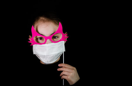 A young girl in a protective mask with a carnival attribute false pink glasses. Portrait of a...