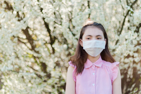 Allergy season. Young girl in medical mask against the blooming apple tree.の写真素材