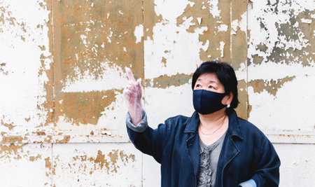 Protection of human face masks in a public place, prevention of coronavirus. Protection against the coronavirus pandemic, flu epidemic. An Asian woman aged about 65 years old in a mask poses.の写真素材