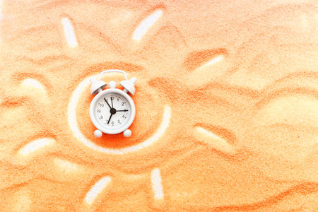 Background summer holidays, the sun painted on the sand, white clock. Concept of summer vacation on...