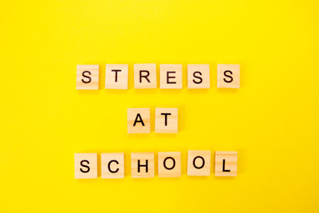 Words stress at school. Wooden blocks with an inscription on top on a yellow background. Social problems of teenagers and children.の写真素材