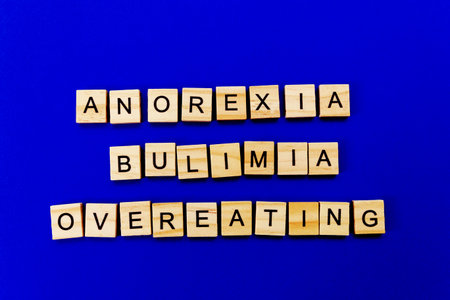 words anorexia, bulimia, overeating. Wooden blocks with an inscription on top on a blue background. Social problems of teenagers.の写真素材