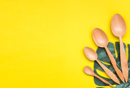 Tableware wooden spoons in a paper Cup and green leaf on yellow background, top view. Zero waste, environmentally friendly concept.の写真素材