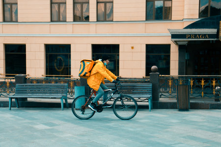 Takeaway food delivery boy on bike with isothermal food case box driving fast. Express delivery of food from cafes and restaurants. Moscow, Russia, June 2020.のeditorial素材