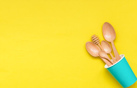Tableware wooden spoons in a paper Cup on yellow background, top view. Zero waste, environmentally friendly concept.の写真素材