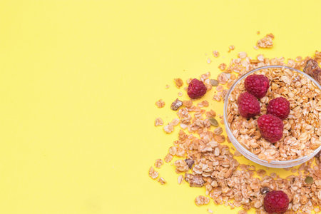 Crispy muesli with raspberry dry Breakfast isolated on yellow background selective focus, top view.