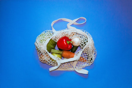 Eco friendly cotton shopper and reusable mesh shopping bag with vegetables on blue background. Selective focus.の写真素材