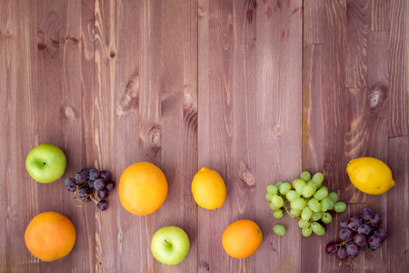 fruit on the bottom edge of a mocha wooden background. lemon, orange, grapefruit, red grapes, green grapesの写真素材