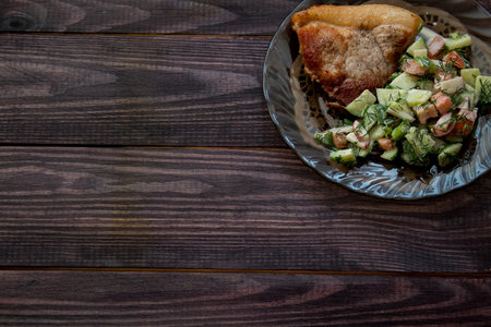 fried pork with vegetable salad of tomatoes and cucumbers with mayonnaise on a wenge-colored wooden...