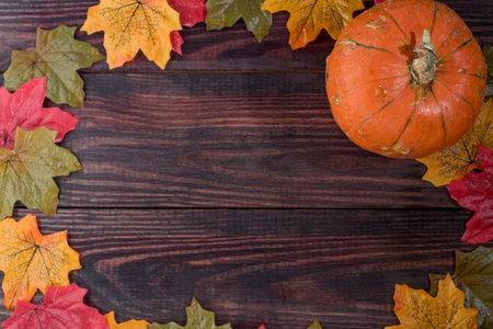 wooden dark background with maple leaves on the edges and pumpkin. space for notesの写真素材