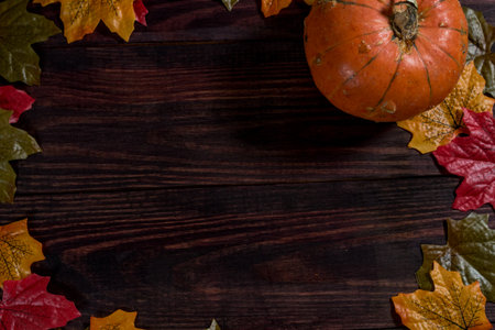 wooden dark background with maple leaves on the edges and pumpkin. space for notesの写真素材