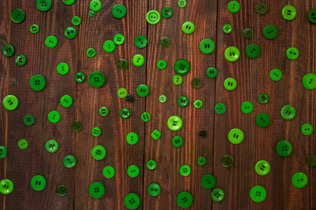 Green buttons of various sizes are scattered over the wooden background. Flatlay
