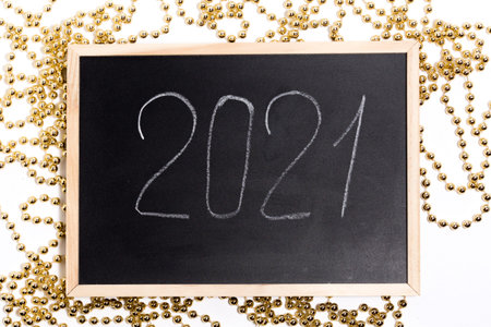 A chalk plaque with the inscription 2021, around the golden beads. New Years Eve