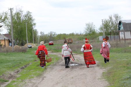 Three women and the teenager in a national dress walk on the village with shovels and a rakeのeditorial素材