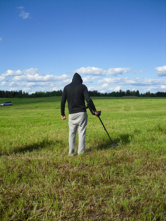 Man enjoying recreational archeology with metal detector in autumn field. Treasure hunt