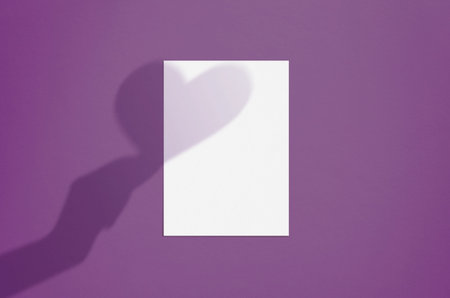 Blank white vertical paper sheet 5x7 inches on liliac background with with hand and heart shadow...
