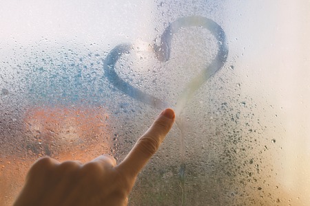 finger on the wet glass draws the heartの写真素材