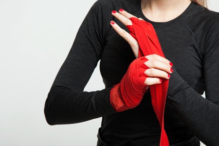 Female boxer is wrapping hands with red boxing wraps. Isolated on white background with space for text. Strong hand and ready for fight, active exercise and sparringの写真素材
