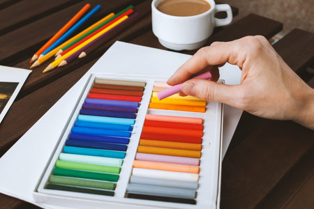 A female hand draws pastel on a white sheet, on a dark table is a cup of coffee