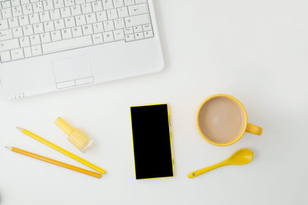 yellow cup, yellow phone, laptop and pencils on white background. Place for text. View from above