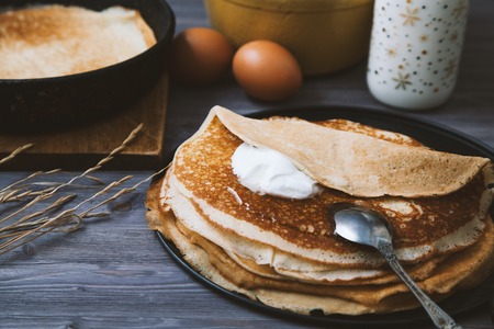 Pancakes in a skillet and ingredients for them on a wooden table.の写真素材