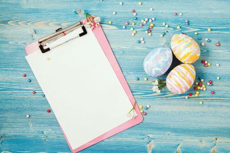 Easter multicolored eggs on a blue wooden background with a tablet and a notebook Background for a...