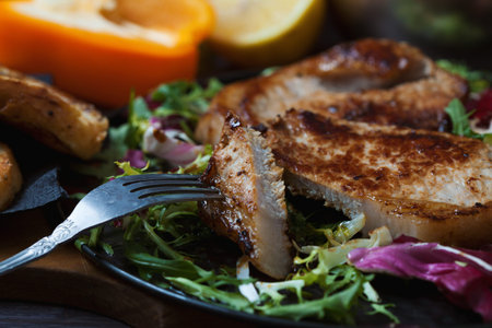 fried meat, a piece of steak on a fork with salad, herbs, pepper, lemon and croutons on a dark...