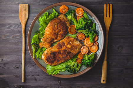 Chicken steak in breadcrumbs with vegetables on a plate.の写真素材