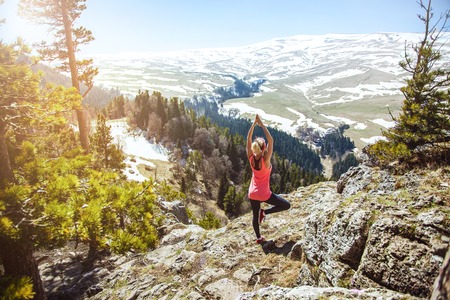 young girl traveler sits on top of a mountain in a yoga pose. The girl loves to travel. Concept for travelers. View from back of the tourist traveler on background mountainの写真素材