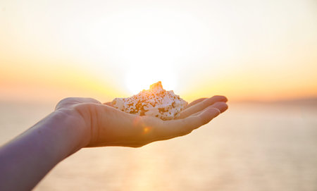 girl holds a cockleshell in the hand at sunset against the sea.