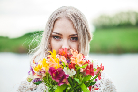 Portrait of a blond girl with a bouquet of flowers on a lake background close-upの写真素材