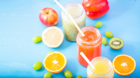 freshly squeezed fruit juice, smoothies yellow orange green blue banana lemon apple orange kiwi grape strawberry on blue backgroundの写真素材