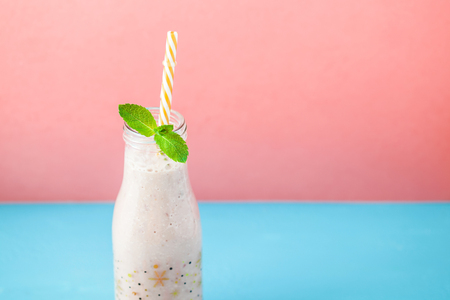 Bottle with smoothie made from milk, cherry, strawberry, banana and decorated with mint on a bright blue. pink backgroundの写真素材