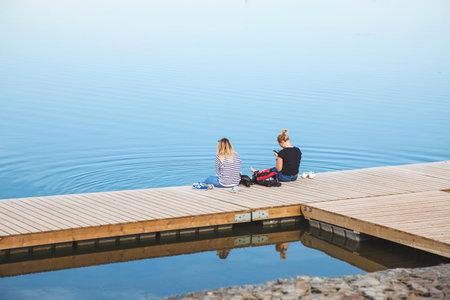 Russia, Rostov-on-Don 03 June 2018 Two girls are sitting on the bridge near the big lakeのeditorial素材