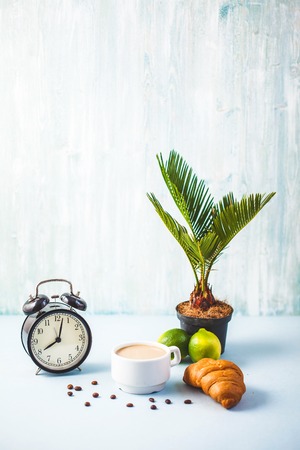 morning breakfast ,coffee in a white cup Croissant Lime on a light background Awakening with an alarm clock Cheerful, healthy breakfast fresh Copy space.の写真素材