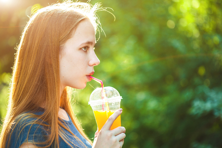young beautiful girl drinks freshly squeezed juice on a background of juicy foliage.の写真素材
