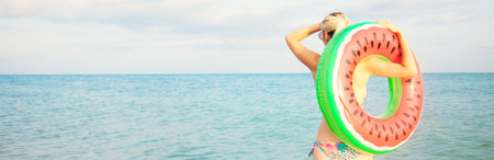 Beautiful girl with inflatable ring stands on the beach and looks at the sea Summer vacation