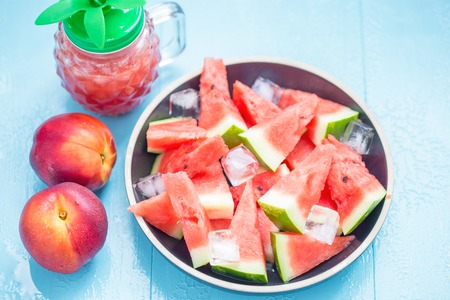 slices of watermelon in a plate with ice and peaches on a blue background Close upの写真素材