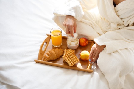 beautiful brunette in a dressing gown and a sweatshirt on her head is having breakfast in bed. Morning conceptの写真素材