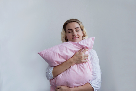 Beautiful blonde girl holds a pillow in her hands. She lies on them with pleasure Copy spaceの写真素材