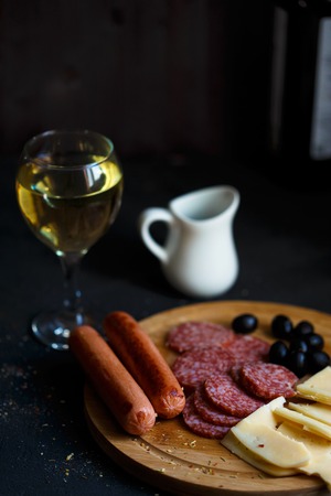 Aperitif table Meat snack, fried sausages, cheese, salami, olives and a glass of wine on a dark table Menu and restaurant concept Close upの写真素材